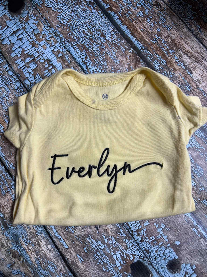 Yellow baby onesie with 'Everlyn' printed on it, using Farmhouse Chic Font.